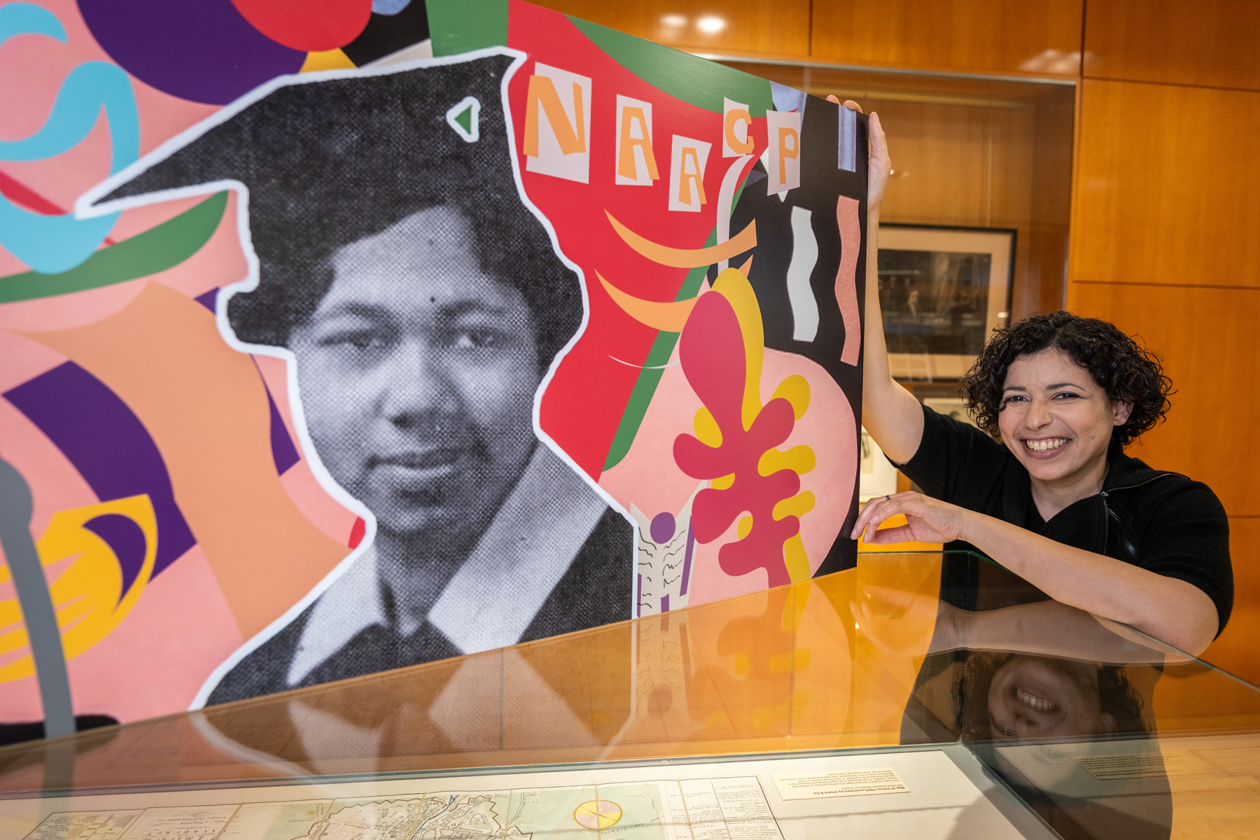 Carli Lowe holding up a colorful collage that is on display in the exhibit.