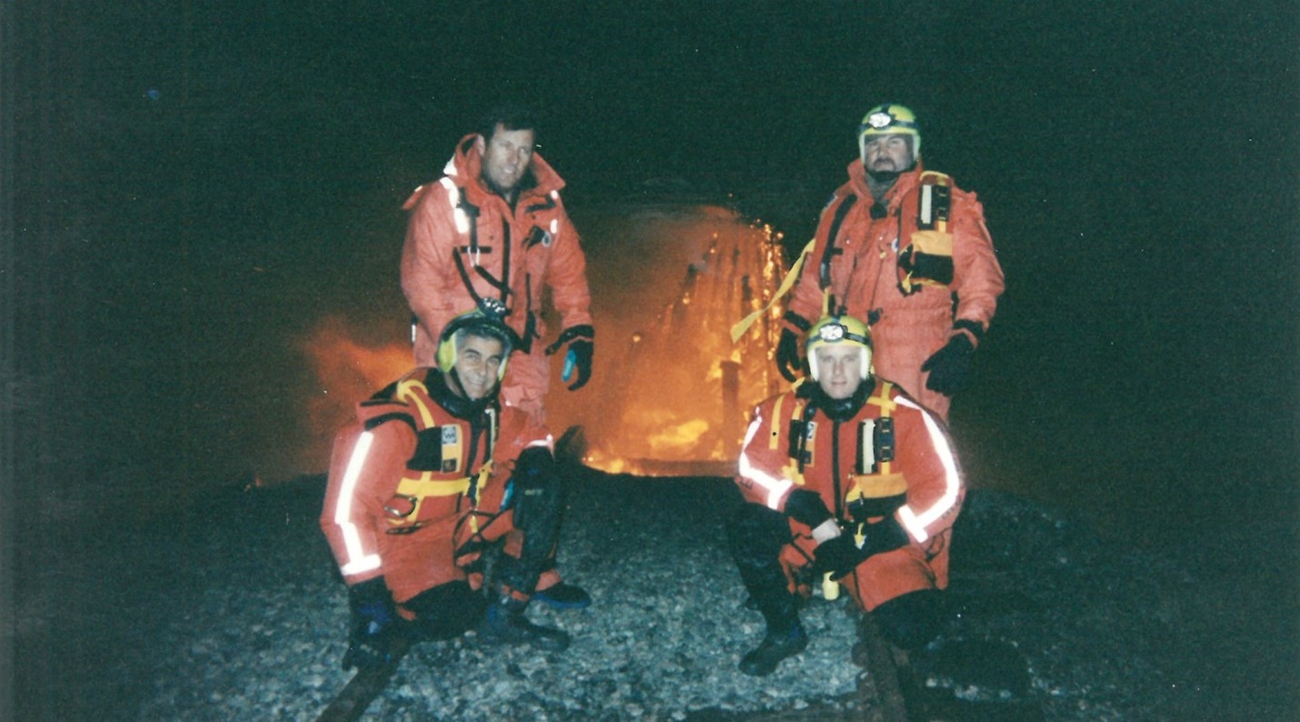 four firefighters pose in front of fire at night