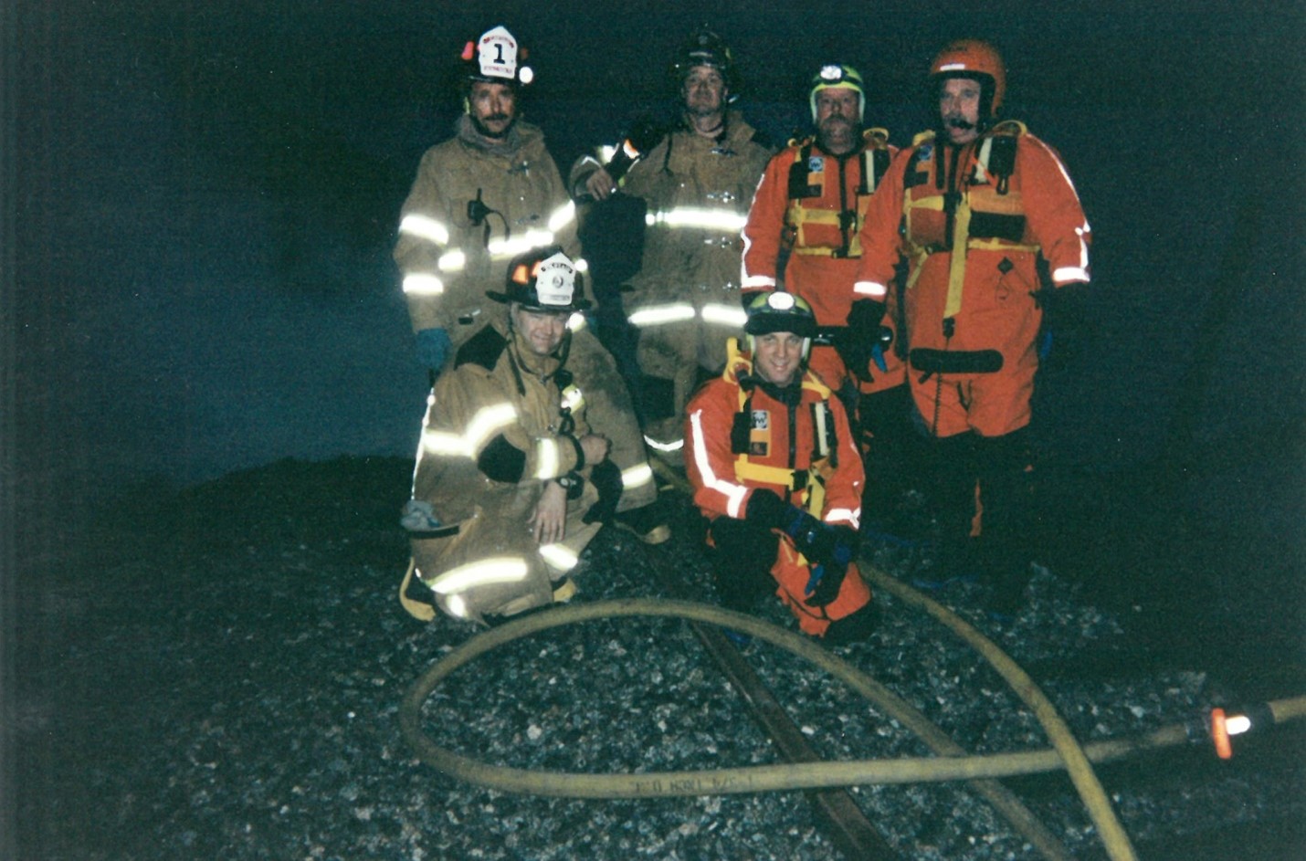 Five firefighters pose in front of smoke at night