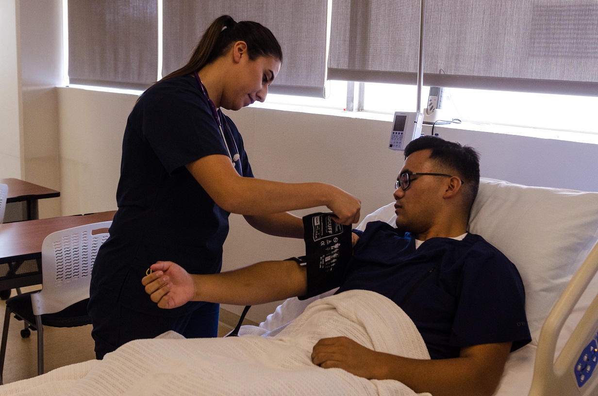 A nursing student practices taking another nursing student's blood pressure.