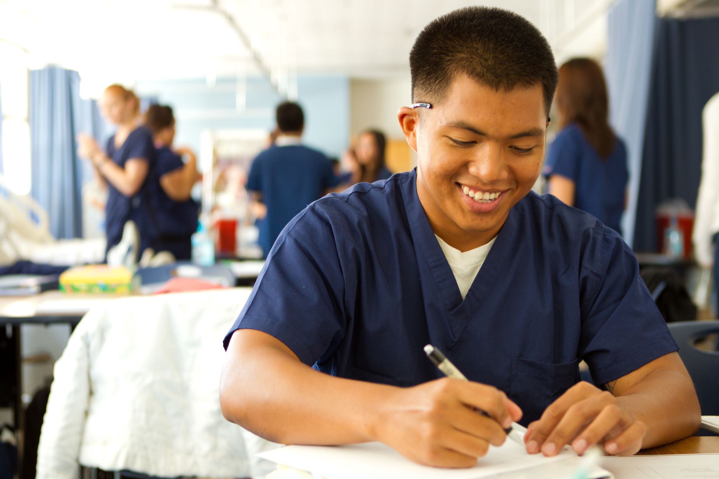 Nursing student in scrubs writes on paper.