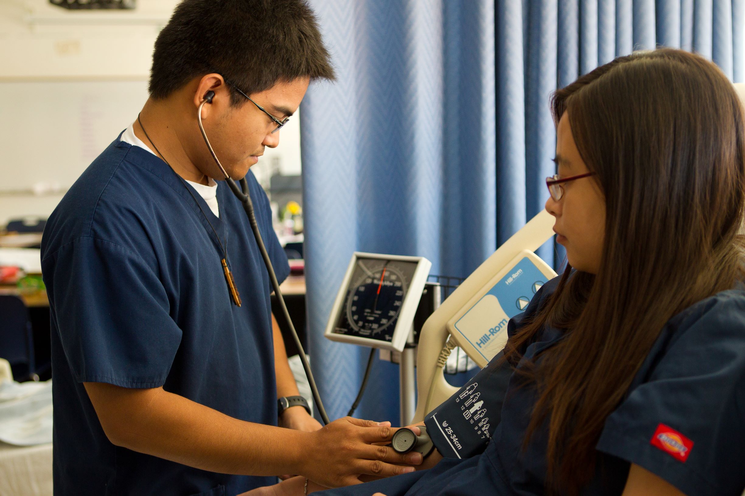 A nursing student practices taking another nursing student's blood pressure.