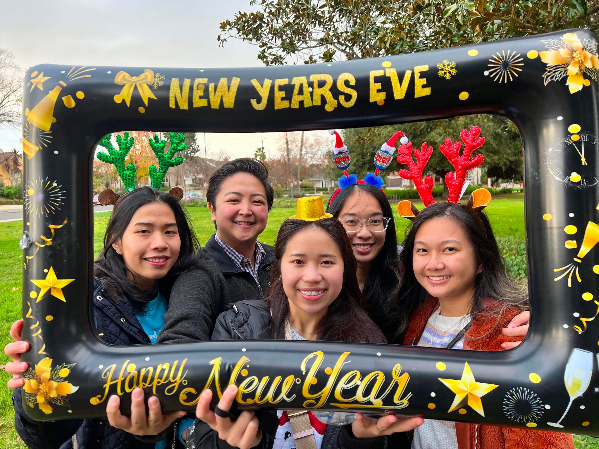 Several CNSA members at a New Years Eve celebration, stading in a grass park, posing with an inflatable picture frame, smiling at the camera.