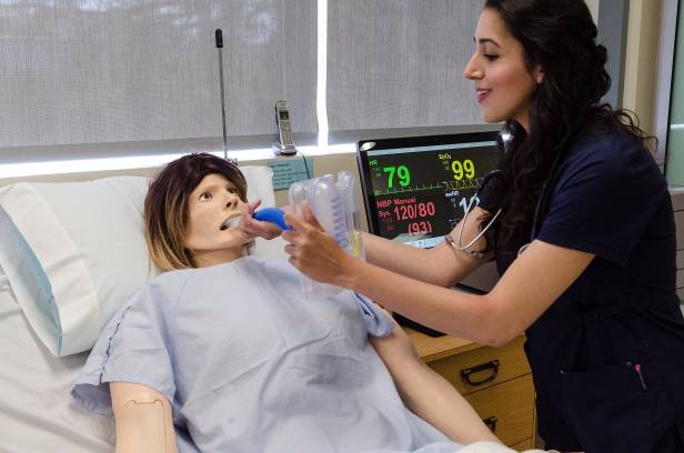 Nursing student in scrubs practices skills on a dummy.