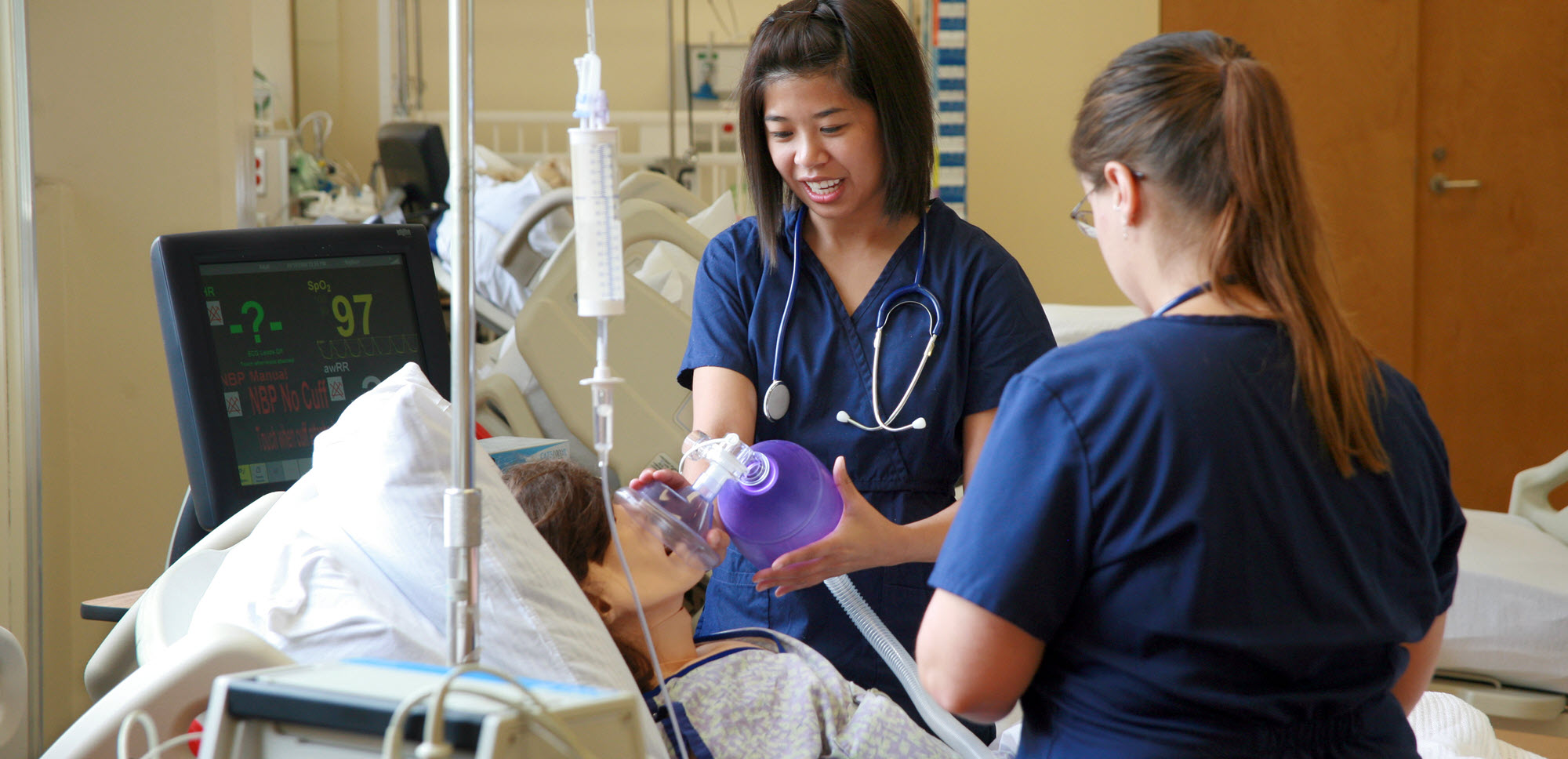 Two nursing students in scrubs practice skills on a dummy during a simulation..