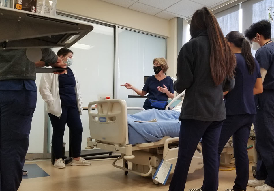 TVFSON nursing instructor leading a class of students, all wearing blue scrubs, in the nursing simulation lab.