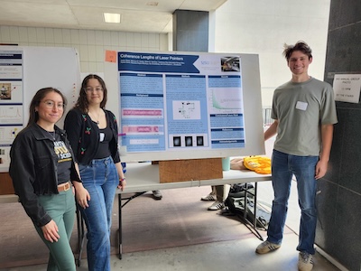 Photograph of students standing in front of a physics poster.