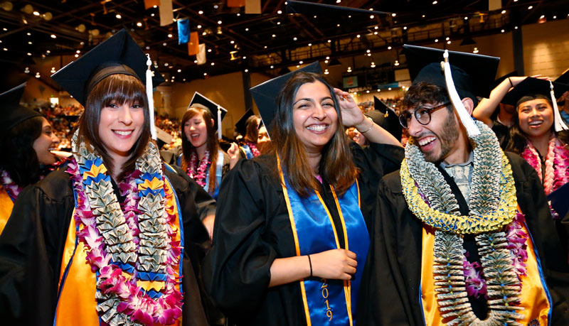 Three graduating students pose in their regalia under the glittering lights of the arena.