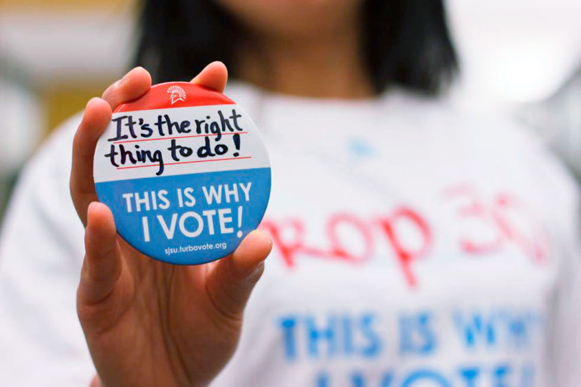 A "this is why I vote" pin being held up by a student.