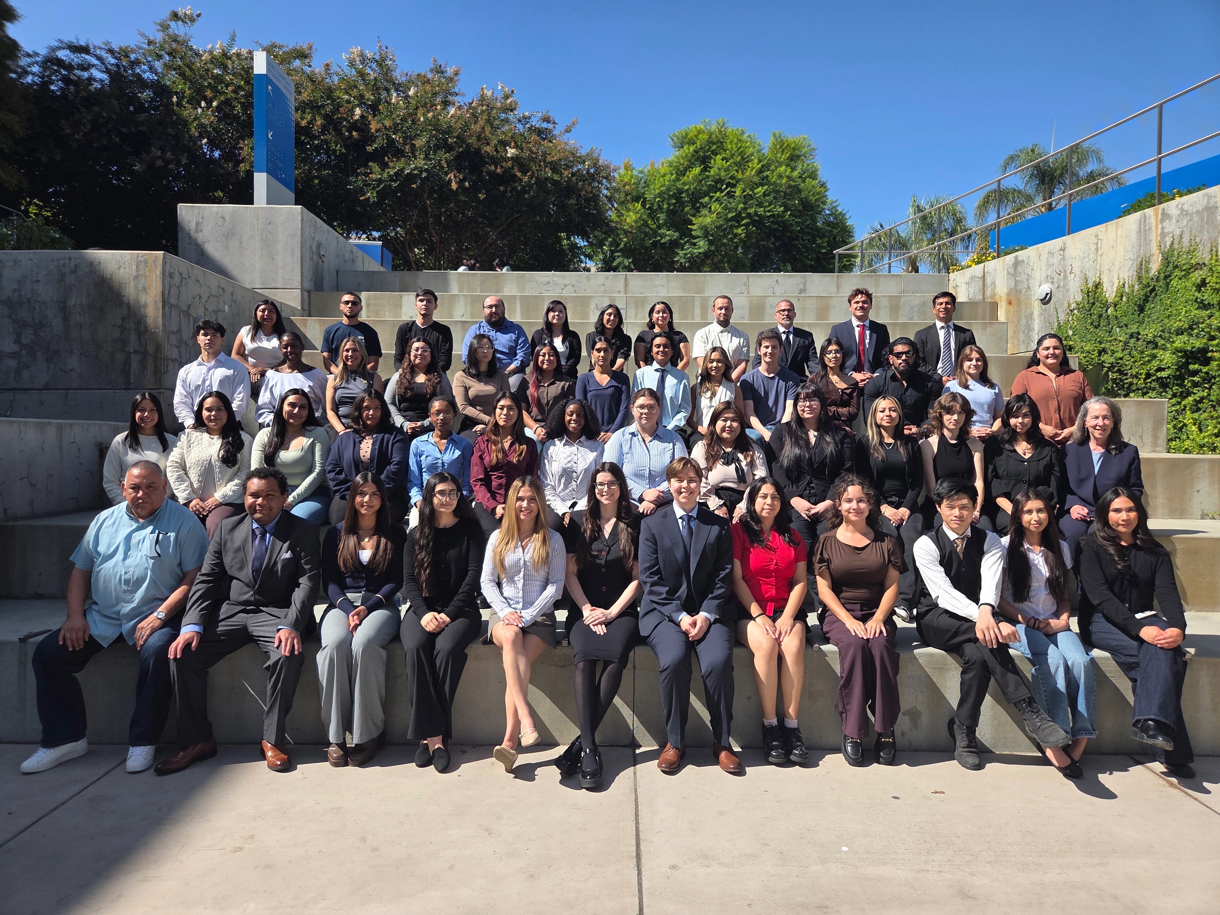 Group of students and a professor, in formal attire, pose for a classroom photo.