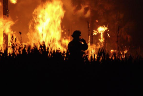 Firefighter standing with wildfire in background