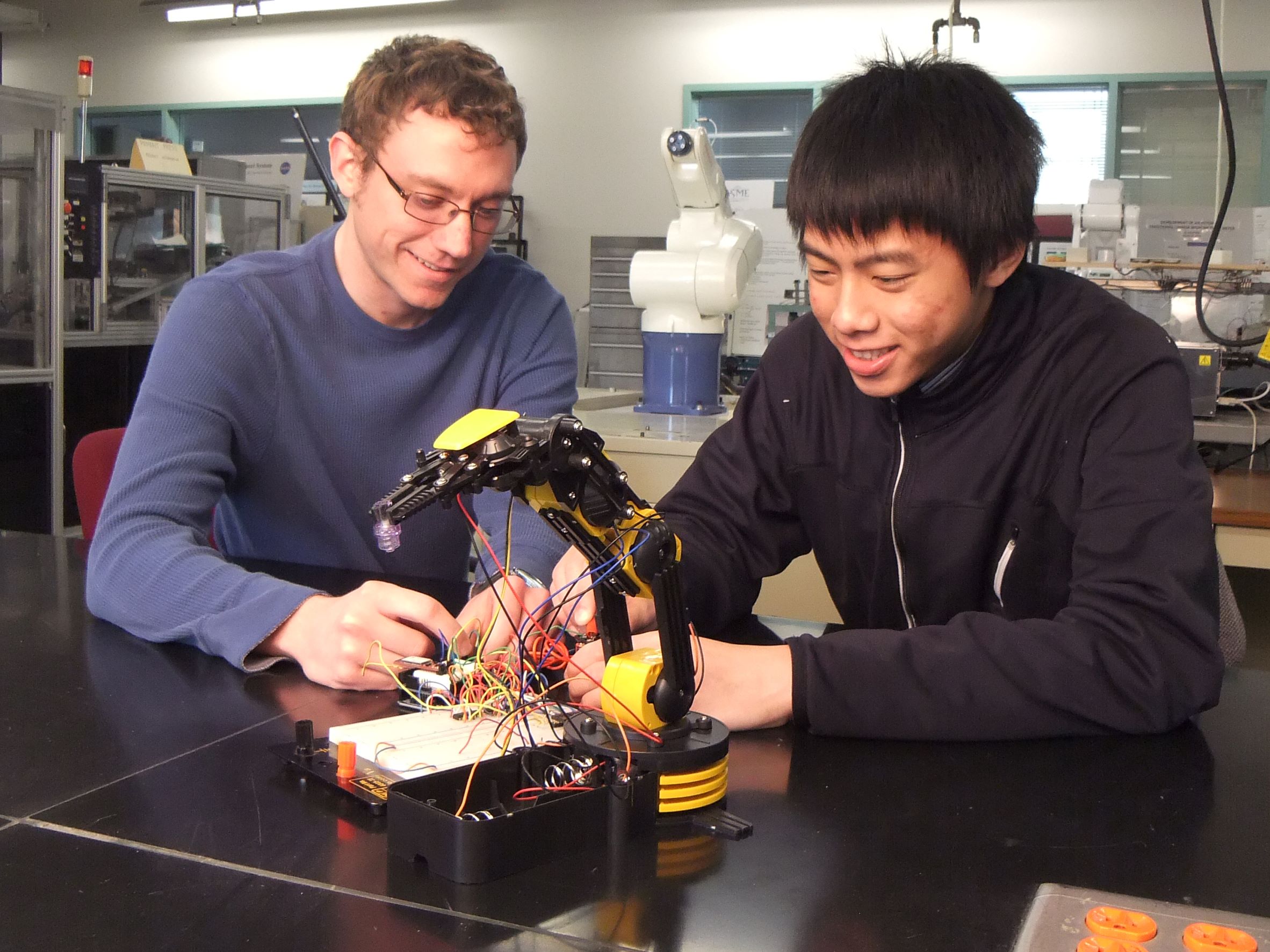 Two men observe a robotic device
