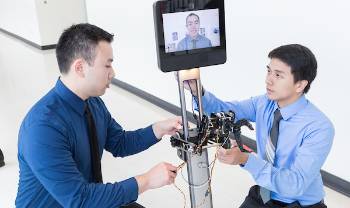 people work on robot with human face on screen