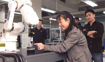 a person holds something near a robot arm with people watching