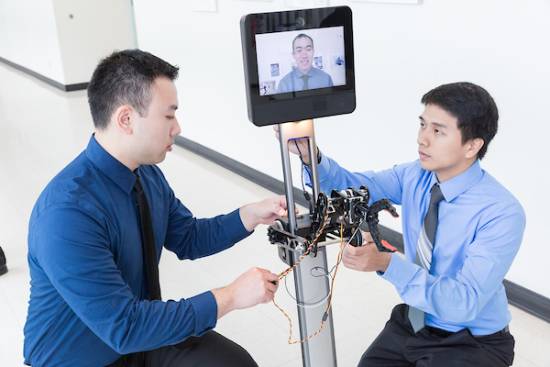two people work on a robot with a human on a screen