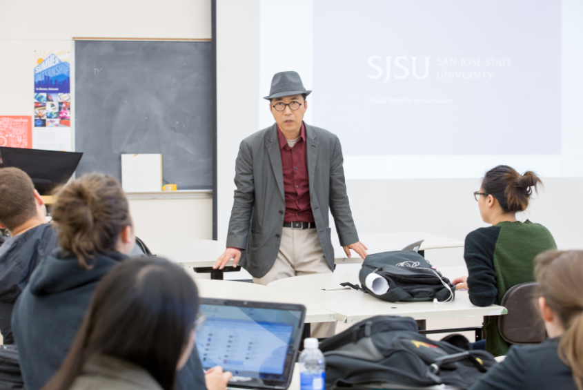 A person standing in a classroom presenting to a group of people