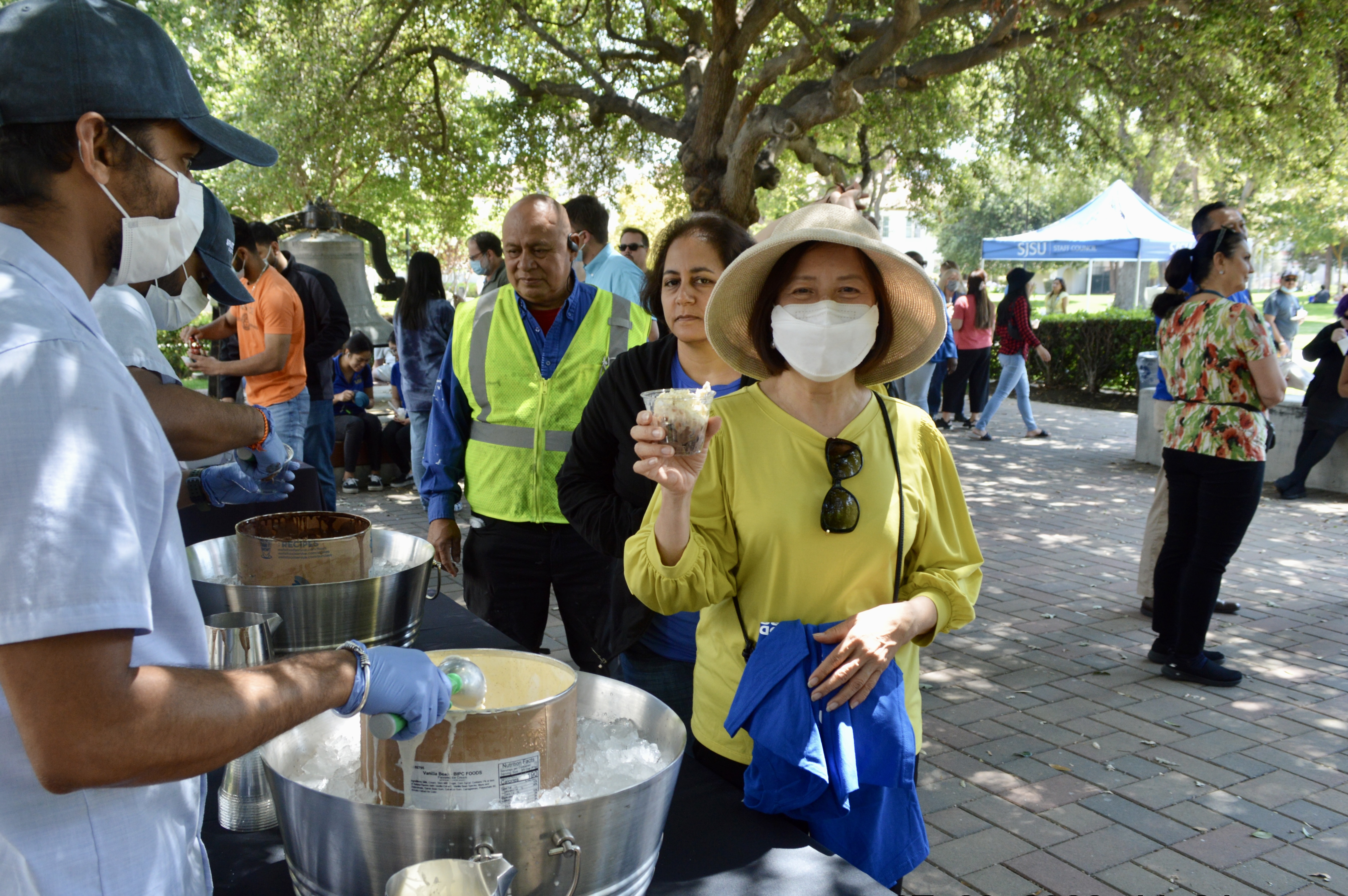 SJSU staff member stands near a table while holding a cup of ice cream.