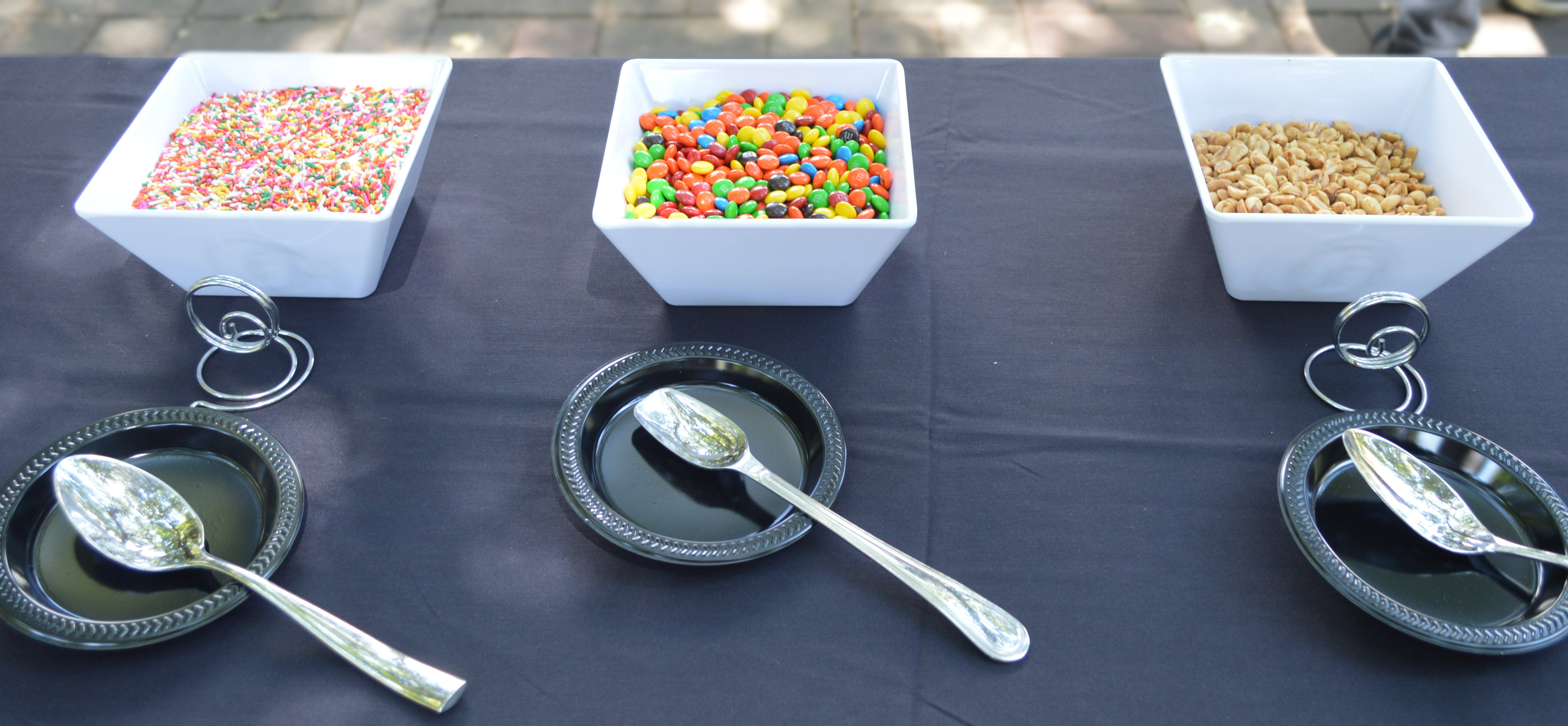 Ice cream toppings in white bowls on a blue tablecloth.