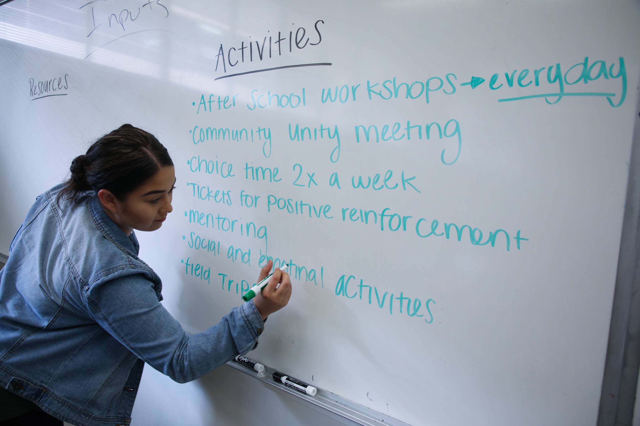 A student writes a list of activities for an assignment on the white board.