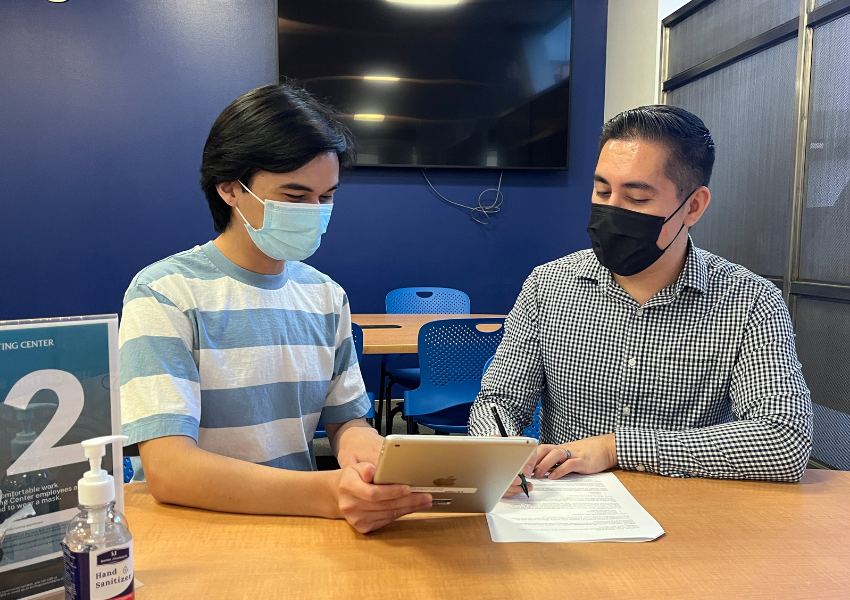 Tutor and student wearing masks sitting at the same table and working on a shared document